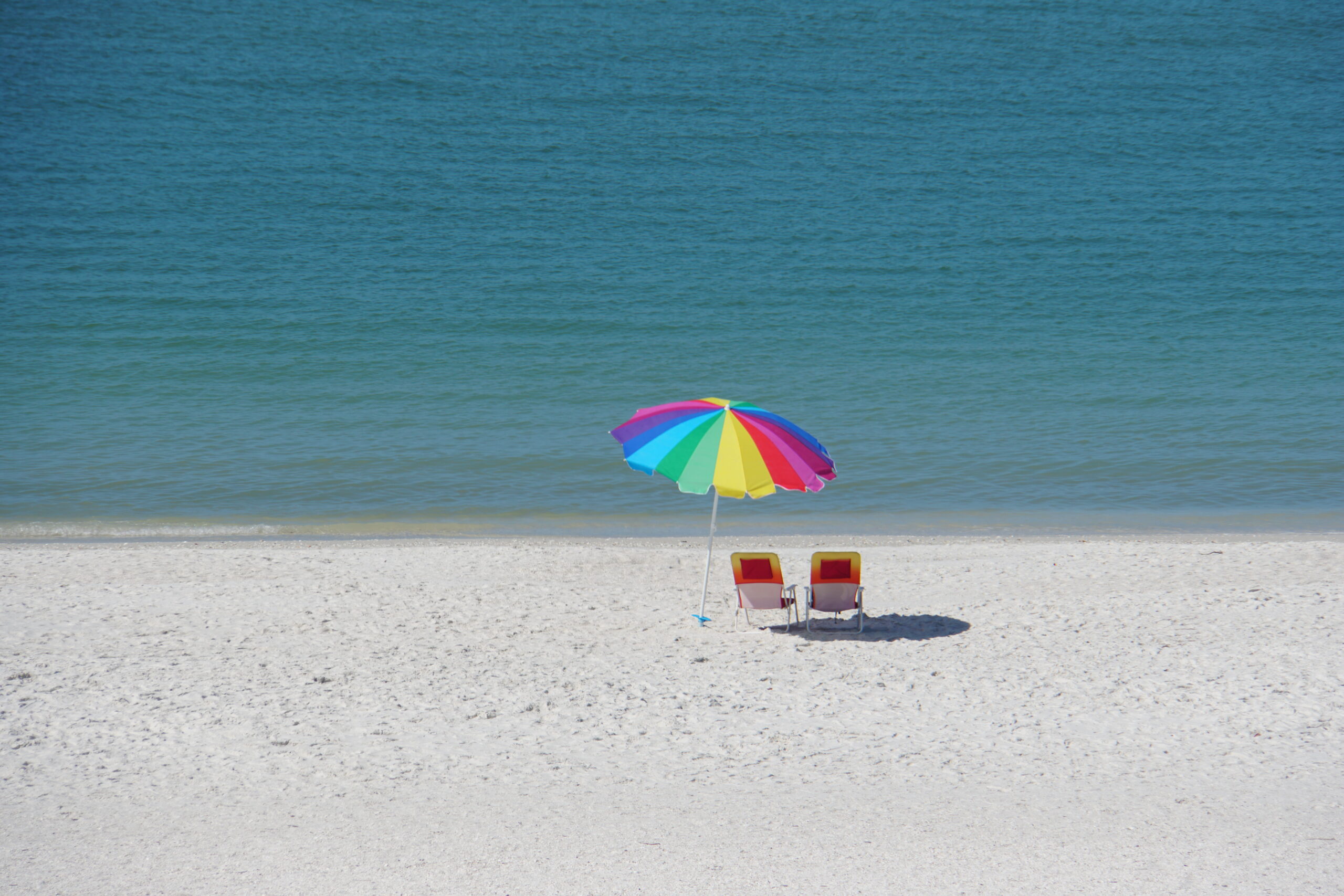 Rainbow umbrella and two beach chairs on bright white sand beside calm Gulf water, Marco Island, Florida