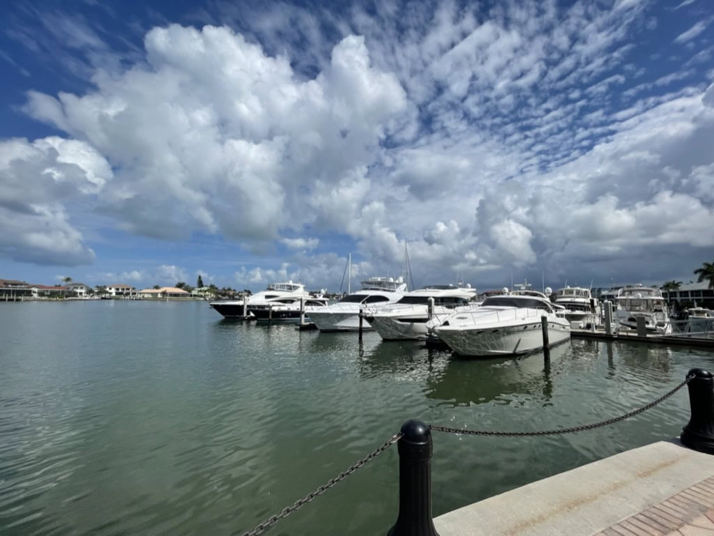 Marina boats docked under dramatic white cumulus clouds on calm water, Marco Island, Florida