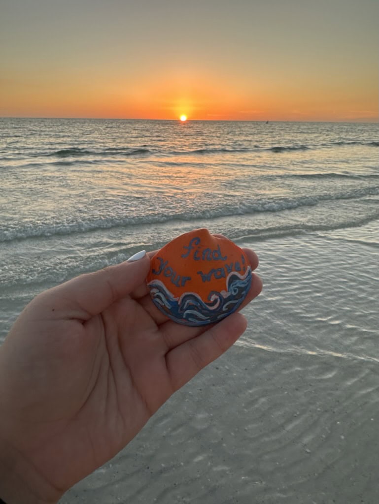 Painted seashell held in front of a glowing Gulf sunset and shallow surf, Marco Island, Florida