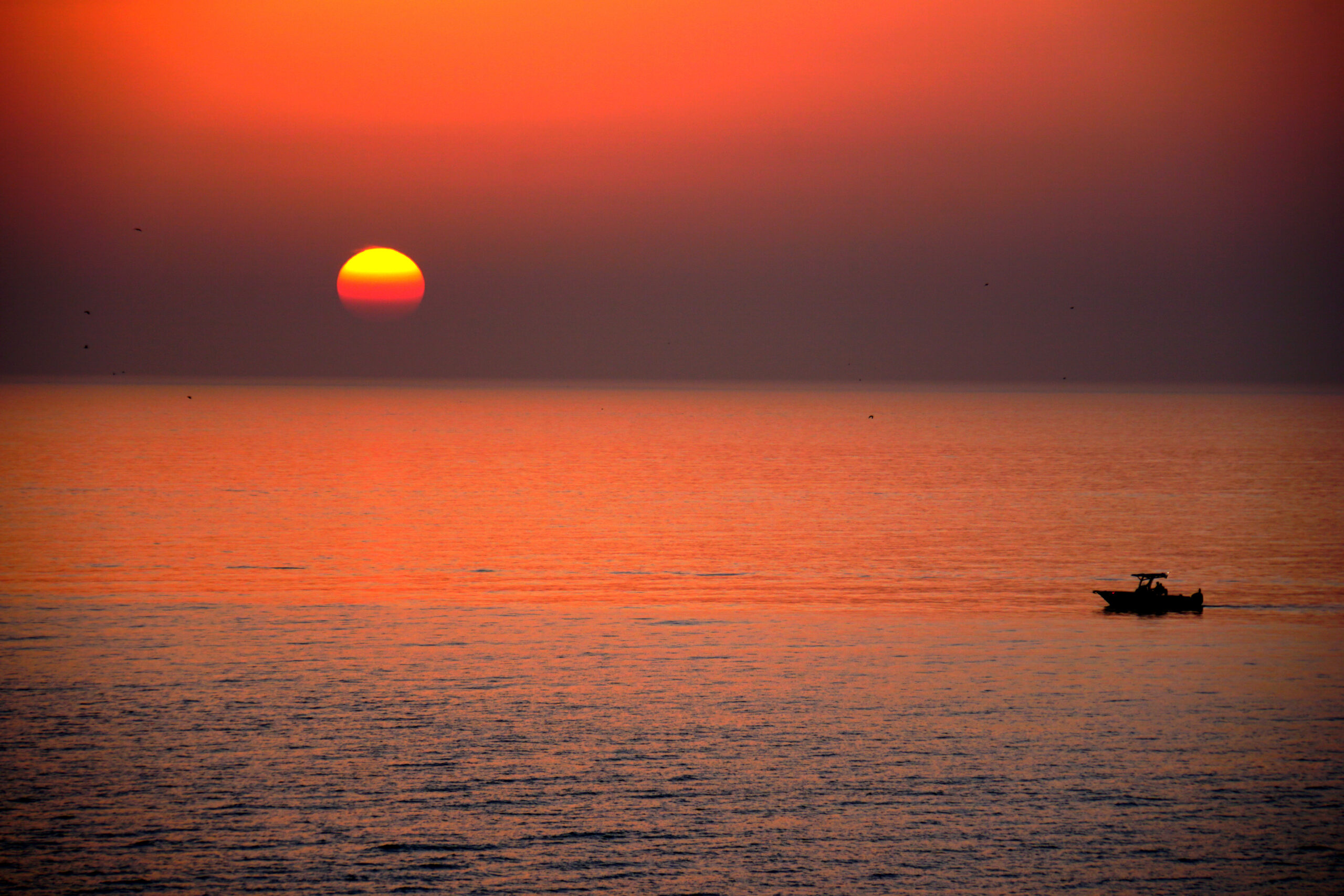 Red-orange Gulf sunset with a small boat silhouetted near the horizon, Marco Island, Florida