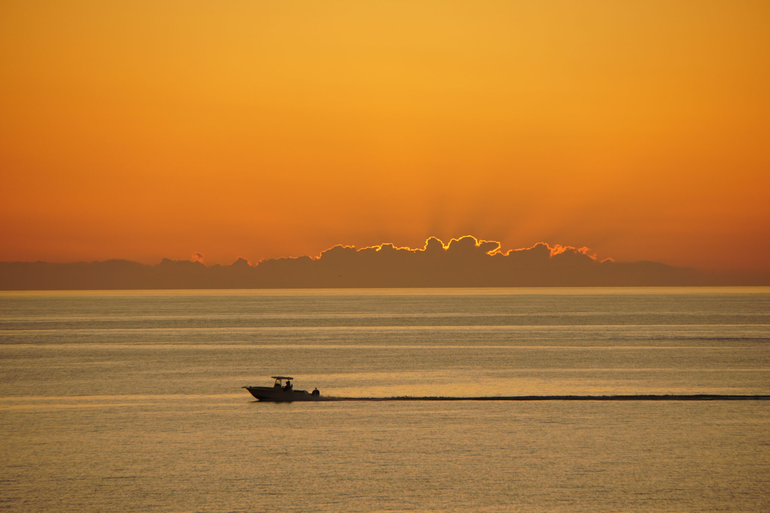 Soft orange sunset behind a low cloud bank with a fishing boat offshore, Marco Island, Florida