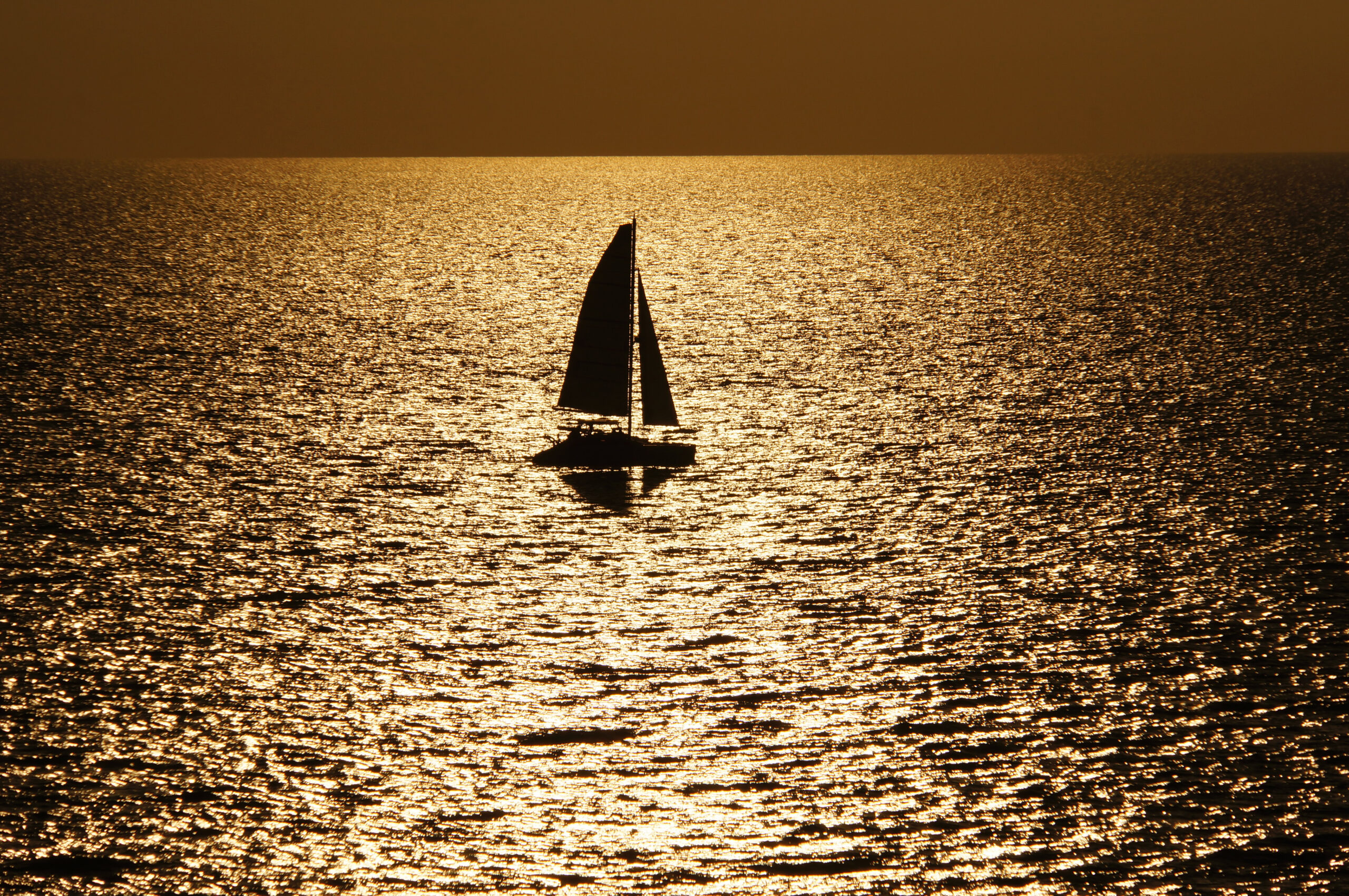 Sailboat silhouetted on sparkling golden Gulf water at sunset, Marco Island, Florida