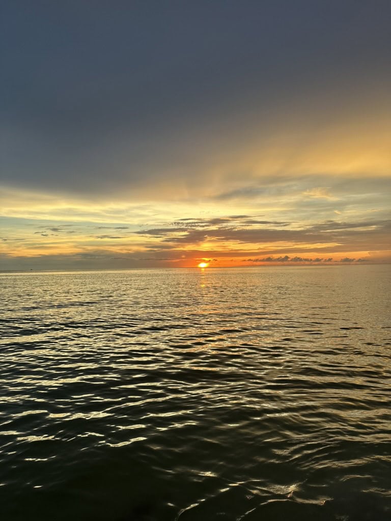Low sun glowing over rippled coastal water beneath soft evening clouds, Marco Island, Florida