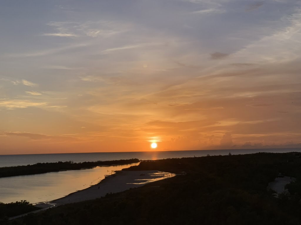 Low orange sun setting over a calm coastal waterway and dark shoreline, Marco Island, Florida